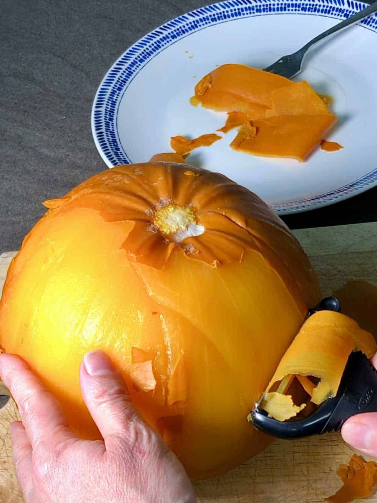 Photo of a pressure cooked instant pot whole pumpkin being peeled effortlessly on a wooden chopping board