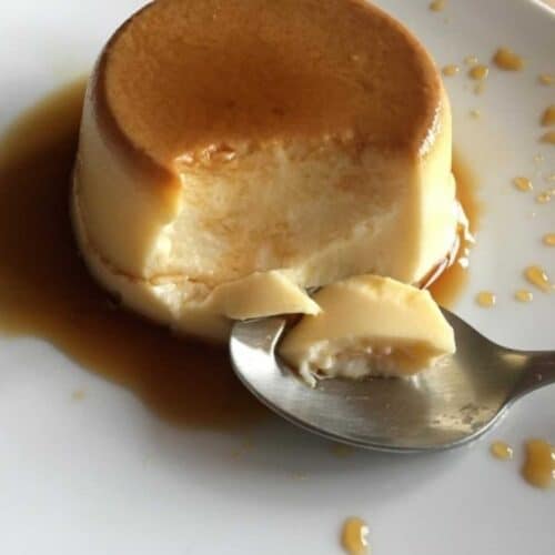 Photo of an Instant Pot Flan de huevo (Spanish Creme Caramel) see on a white plate with specks of caramel, a spoon has take a bit off showing the lovely middle