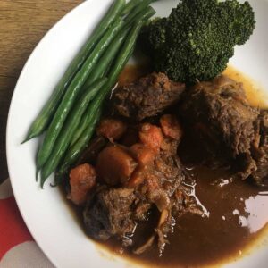 Photo of the Instant Pot Ox Cheeks in Stout seen from above served on a white plate with some green beans on the top left and also some broccoli top right