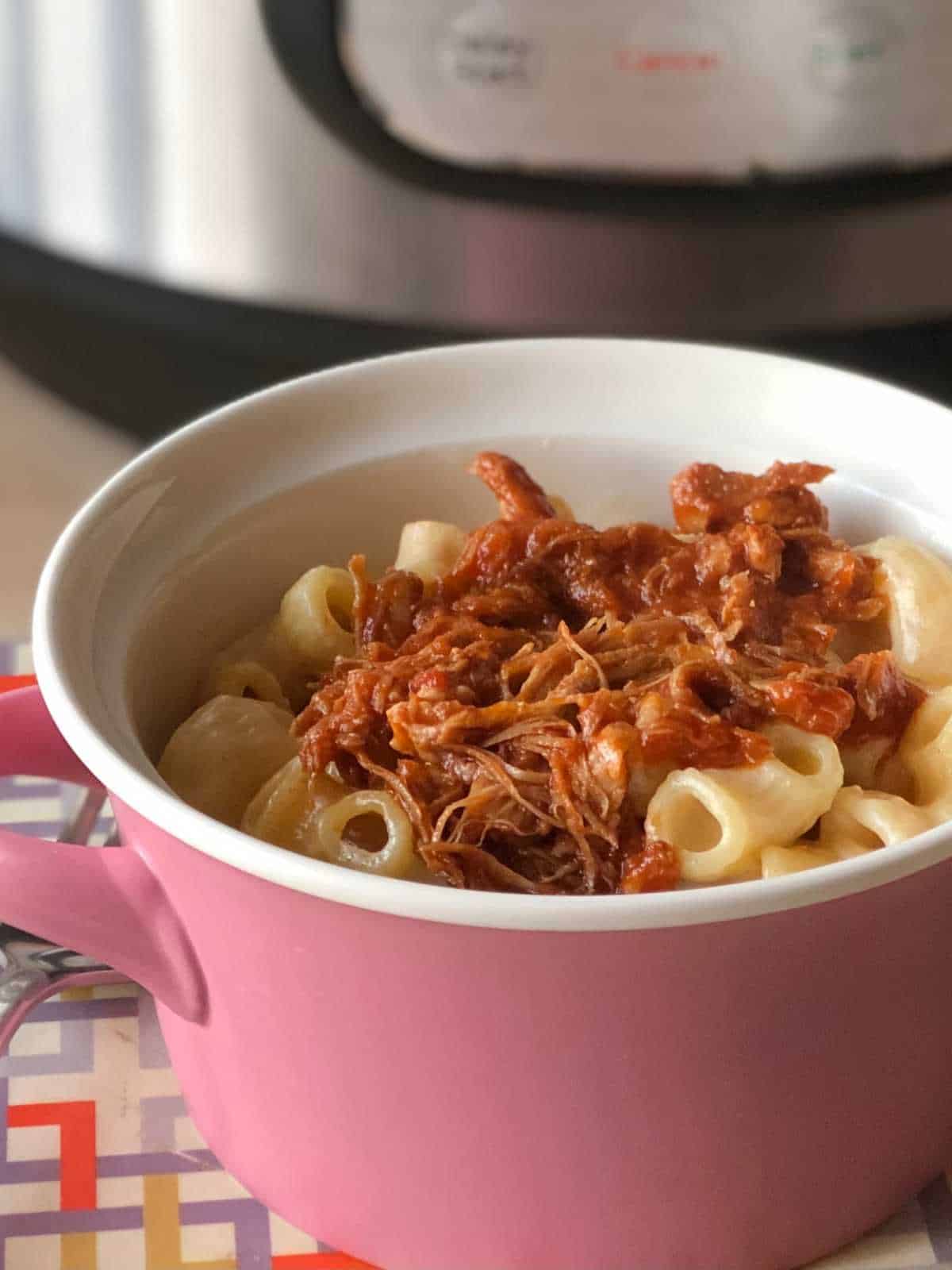 Photo of Jayson's Mac and Cheese served in a pink pot with handles topped with pulled pork, with an Instant Pot in the background