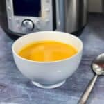 Photo of the bright orange soup seen inside a white bowl with an Instant Pot Duo Evo Plus in the background