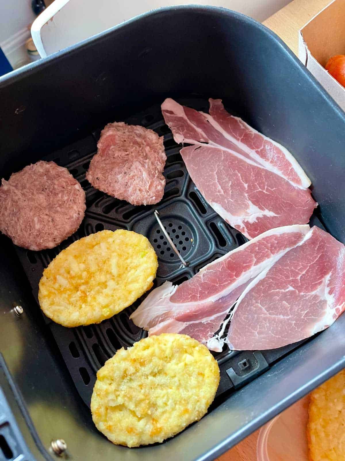 photo of Step 1 of air fryer McMuffins - ingredients seen in air fryer basket of Instant Vortex - hash browns, bacon rashers, sausage patties