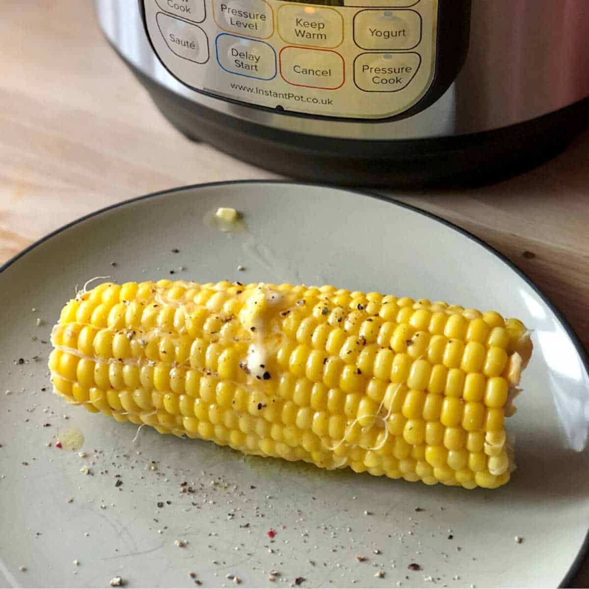 Photo of the pressure cooked sweetcorn on the cob on a plate with an Instant Pot Duo Mini at the back