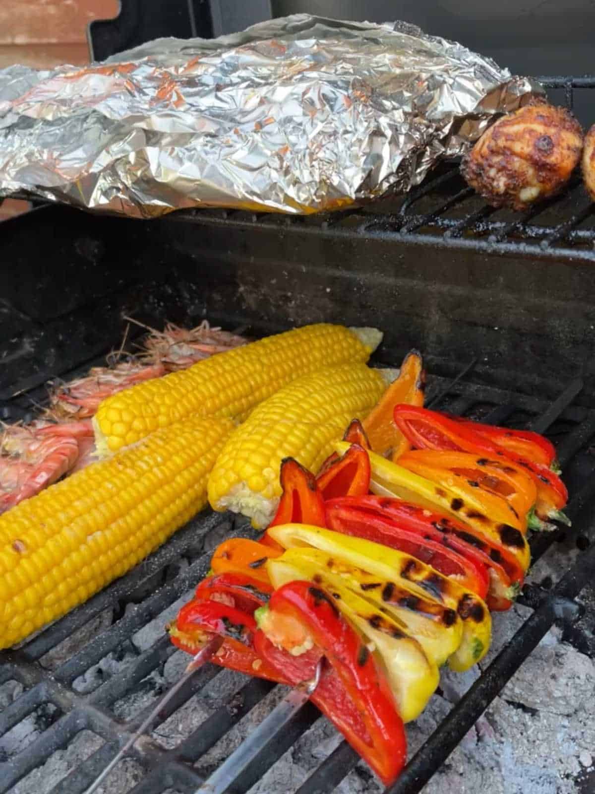 Photo of pressure cooked sweetcorn on the cob popped on the BBQ grill surrounded by peppers and prawns