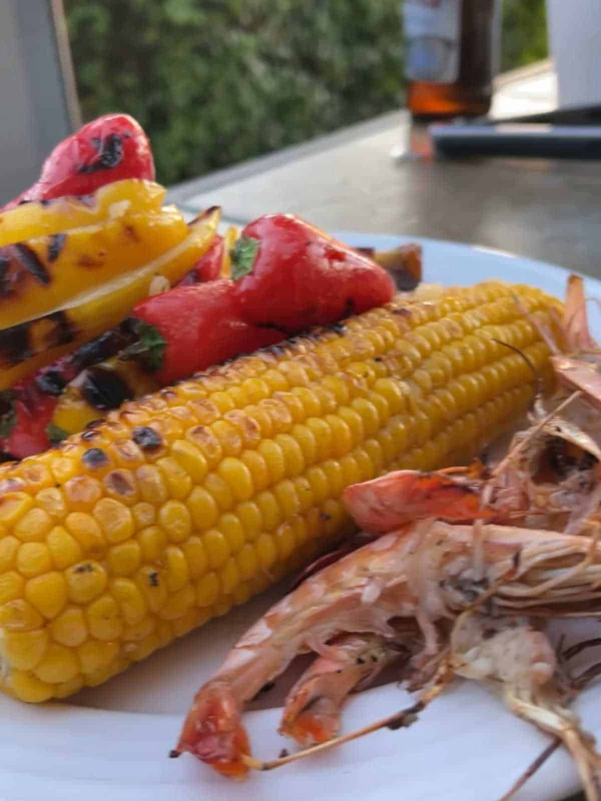 Photo of the corn on the cob seen on a plate with prawns and peppers after chargrilling on the BBQ