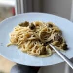 Photo of a white plate with creamy tuna pasta being held up by an arm in a grey sweater