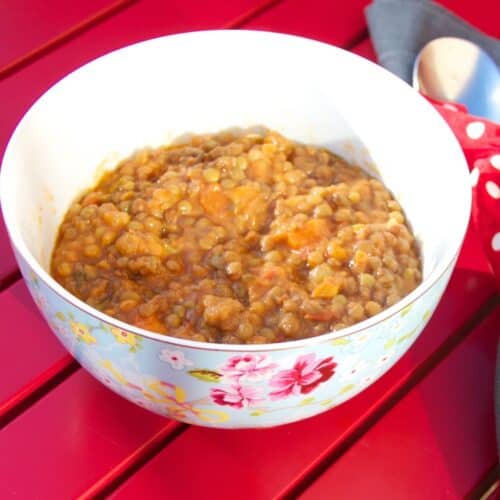 Photo of the thermomix Spanish lentejas lentil stew seen in a pretty blue flowery bowl, with a red slatted table as the background