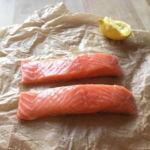 Photo of two salmon steaks on a wet surface with half a lemon in the background
