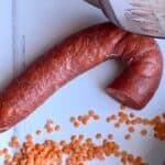 Photo of a chorizo sausage loop with a bit cut off seen from above on a white surface surrounded by dried red lentils and an Instant Pot Duo