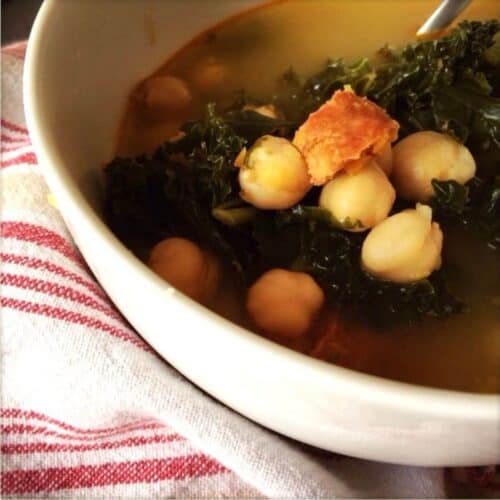 A photo of the delicious soup served in a white bowl with a tea towel underneath, you can clearly see the kale , chorizo and chickpeas