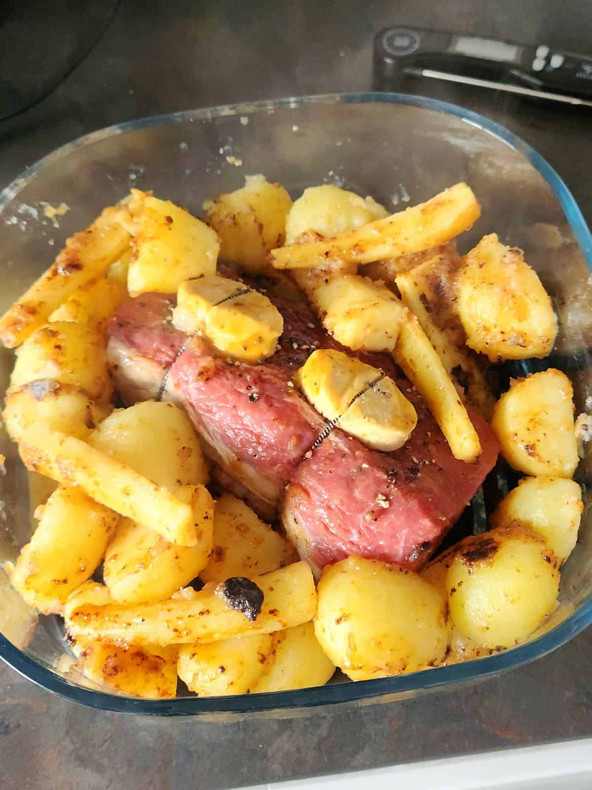 The beef joint surrounded by the parboiled potatoes and parsnips tinged by the oxo cube