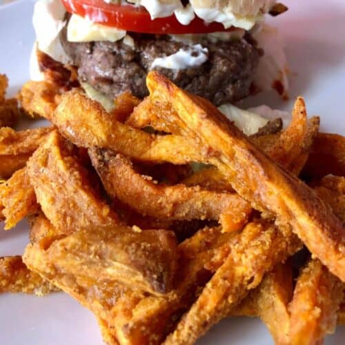 Image of the Sweet Potato Fries air fried in the Instant Pot Duo Crisp and served on a white plate with a burger in the background