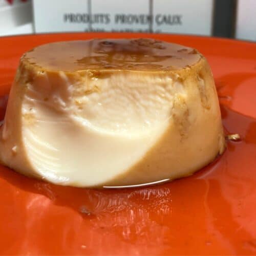 Photo of a pressure cooked flan de Huevo Creme Caramel served on an orange plate, one bite has already been eaten so the smooth inside is showing, there's delicious caramel too