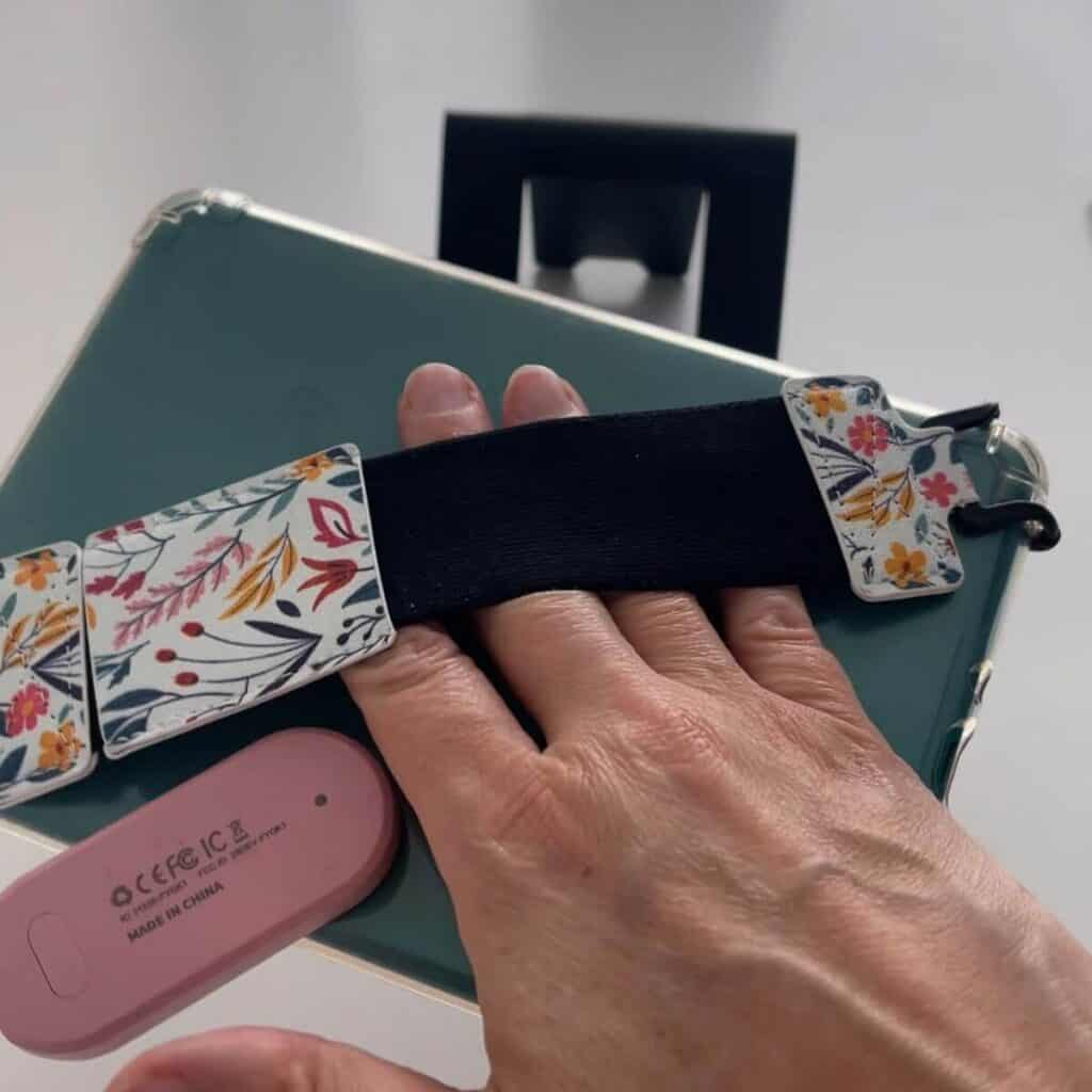 Photo of a floral kindle strap for easy holding, it's attached to a teal kindle paperwhite