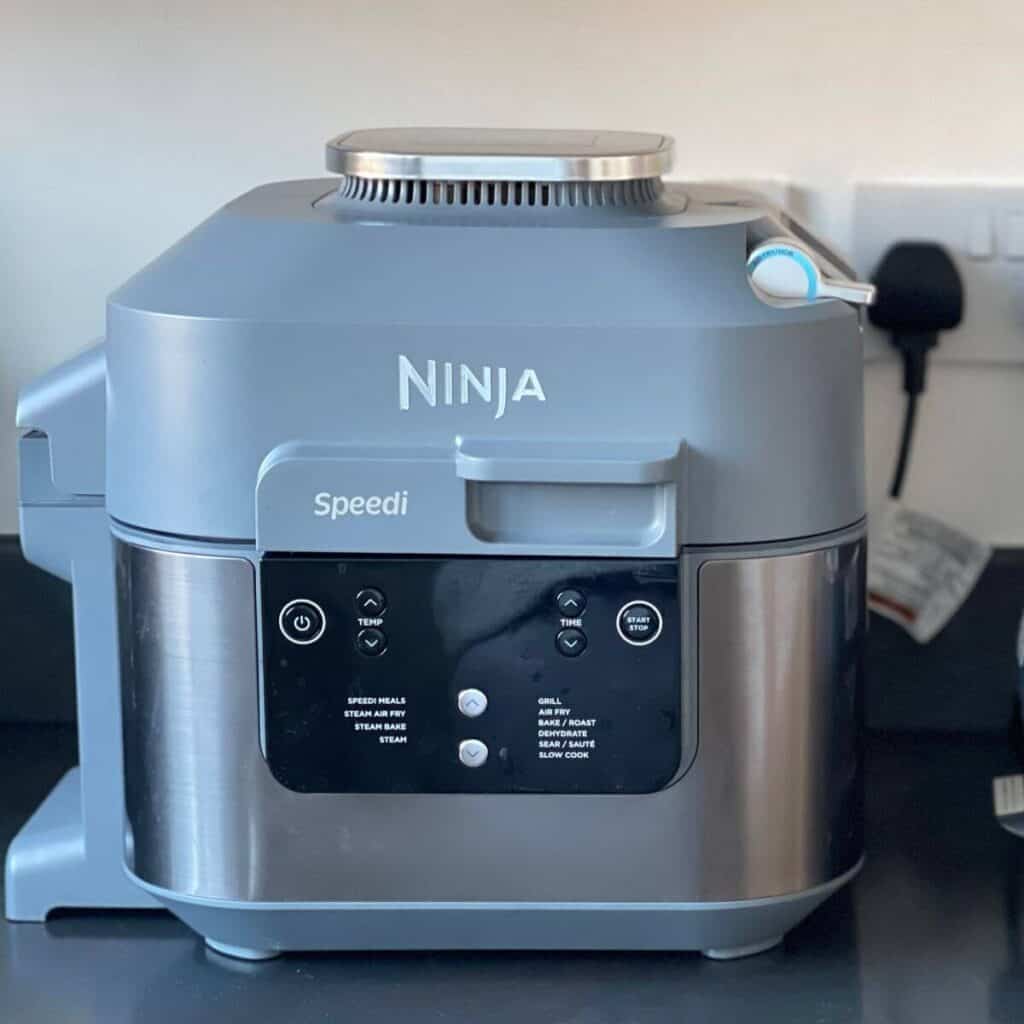 Photo of a Ninja Speedi on a dark kitchen counter, it's plugged into a socket in the background