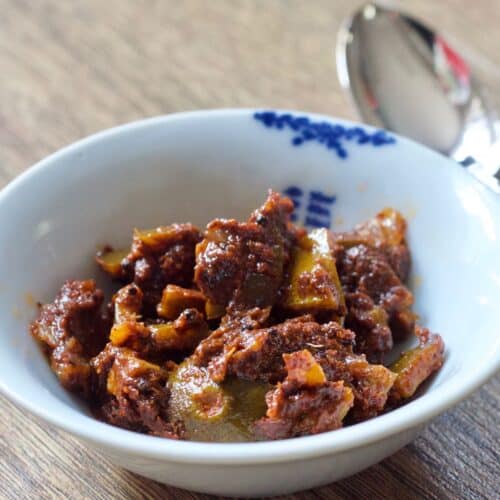 Photo of a white bowl containing lime pickle, there's a spoon on the top right of the image