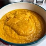 Photo of the Roast Pumpkin Soup served in a bowl, there is a small metallic container with the word Baharat on it on the top right