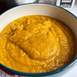 Photo of the Roast Pumpkin Soup served in a bowl, there is a small metallic container with the word Baharat on it on the top right