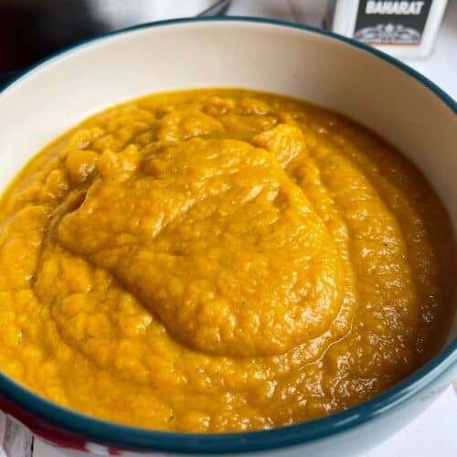Photo of the Roast Pumpkin Soup served in a bowl, there is a small metallic container with the word Baharat on it on the top right
