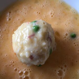 Photo of an arancini rice ball coated in beaten egg