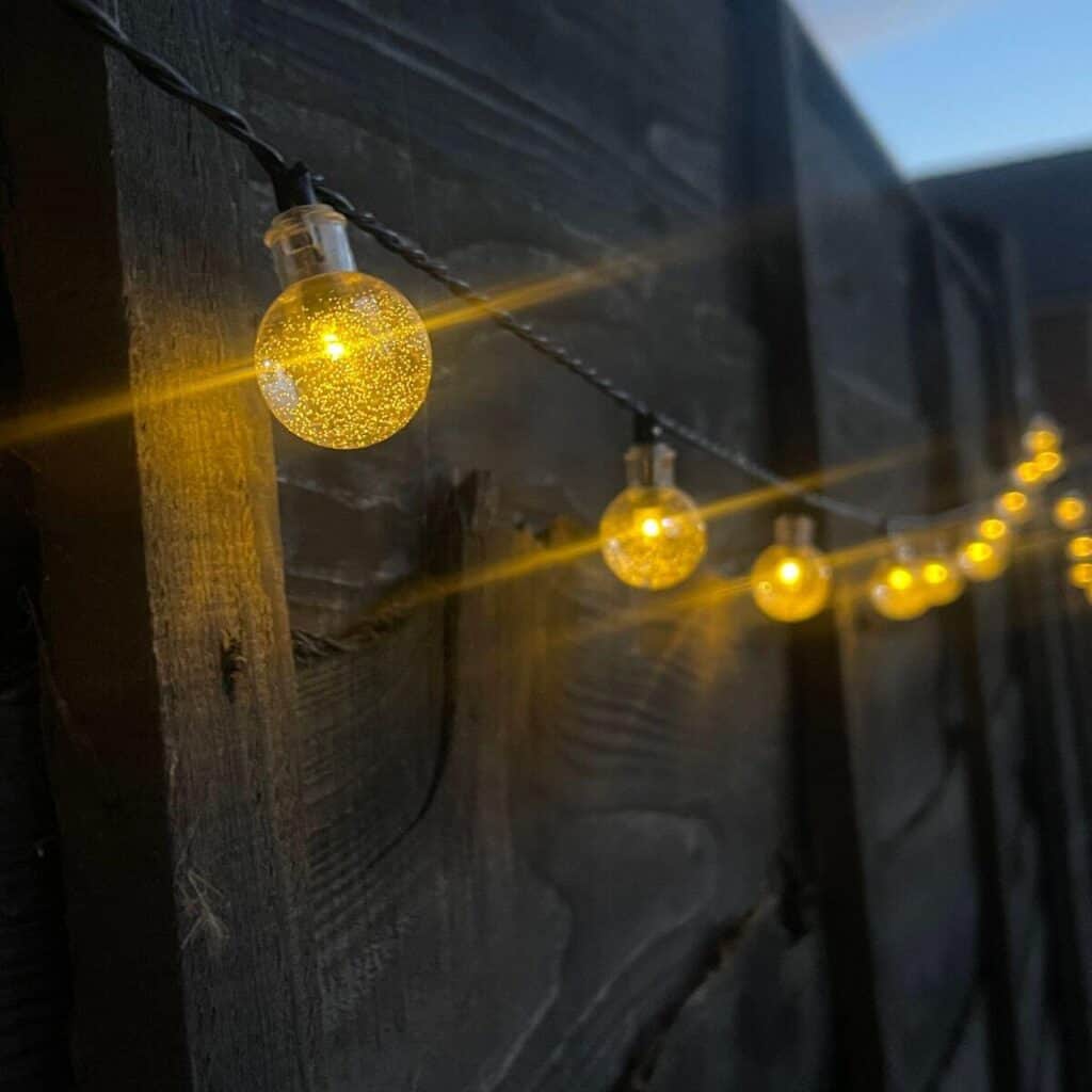 Photo of solar fairy lights along a fence, the sky is dark and they are lit up