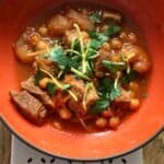 Lamb tagine served in an orange bowl and topped with fresh herbs and lemon zest
