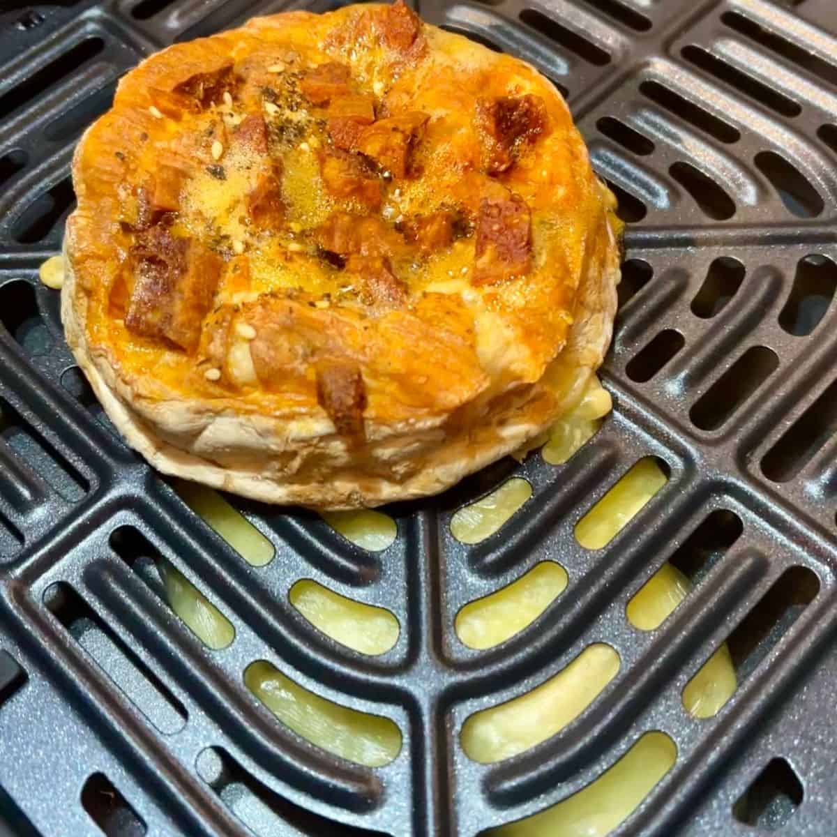 whole camembert in air fryer drawer with leaked melted cheese underneath