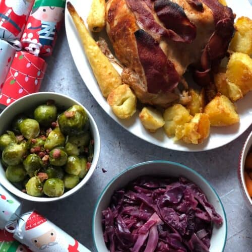 Pressure cooked Turkey crown, roast potatoes and parsnips served in an white dish with a bowl with Brussels sprouts and another with red cabbage