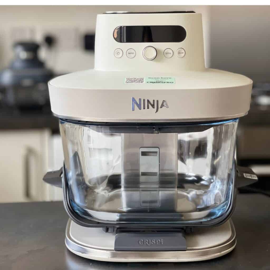 A white Ninja Crispi Pro on a dark kitchen counter. The standard Ninja Crispi is in the background on the left